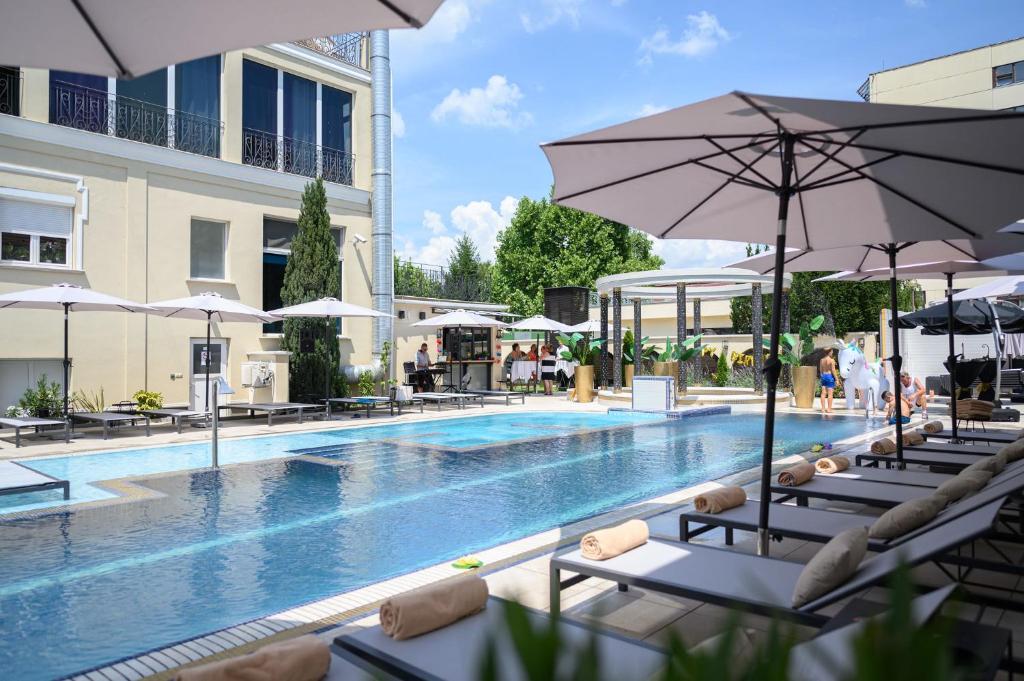 einen Pool mit Stühlen und Sonnenschirmen neben einem Gebäude in der Unterkunft Hotel Aurum in Hajdúszoboszló