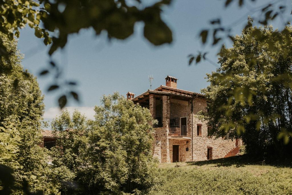 una vecchia casa in pietra con alberi in primo piano di Can Roca Rural a Sant Joan de les Abadesses