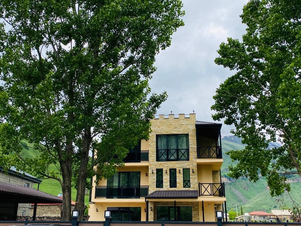 a yellow building with trees in front of it at Besami Hotel in Stepantsminda