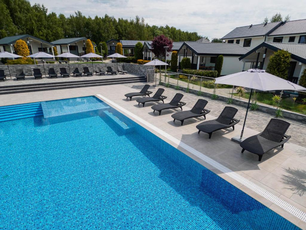 a swimming pool with chairs and umbrellas next to a swimming pool at Domki Alan Jarosławiec in Jarosławiec