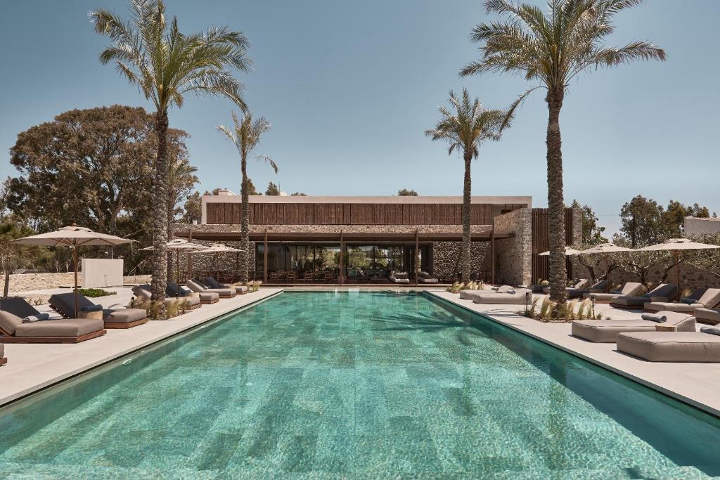 a swimming pool with lounge chairs and palm trees at Theros All Suite Hotel - Adults Only in Kos