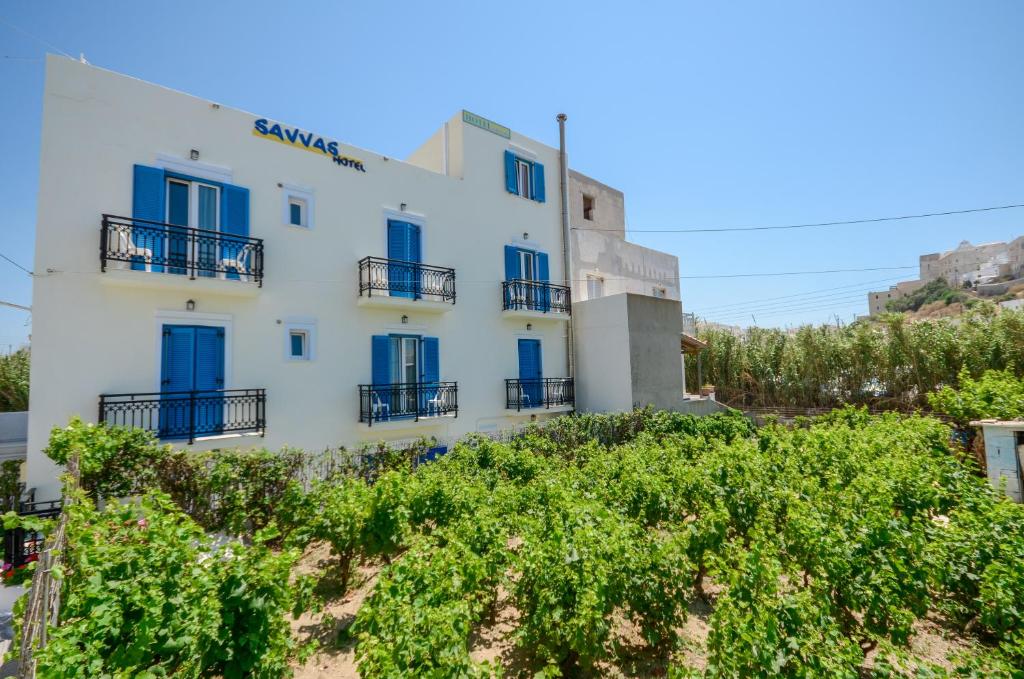 a white building with blue windows and bushes at Naxos Hotel Savvas in Naxos Chora