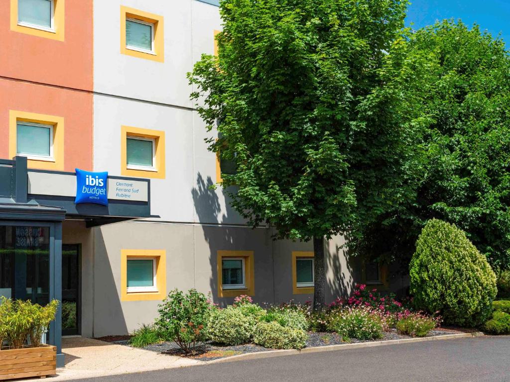 a building with a tree in front of a street at ibis budget Clermont Ferrand Sud in Aubière