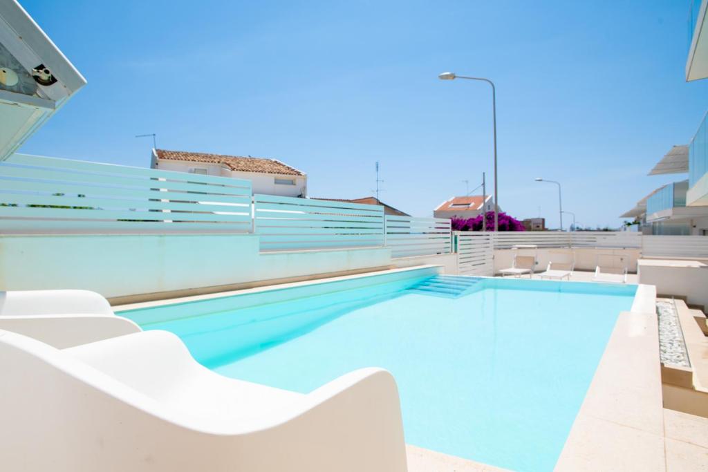 una piscina con sillas blancas junto a un edificio en DELPOSTO Marina di Ragusa PRL, en Marina di Ragusa