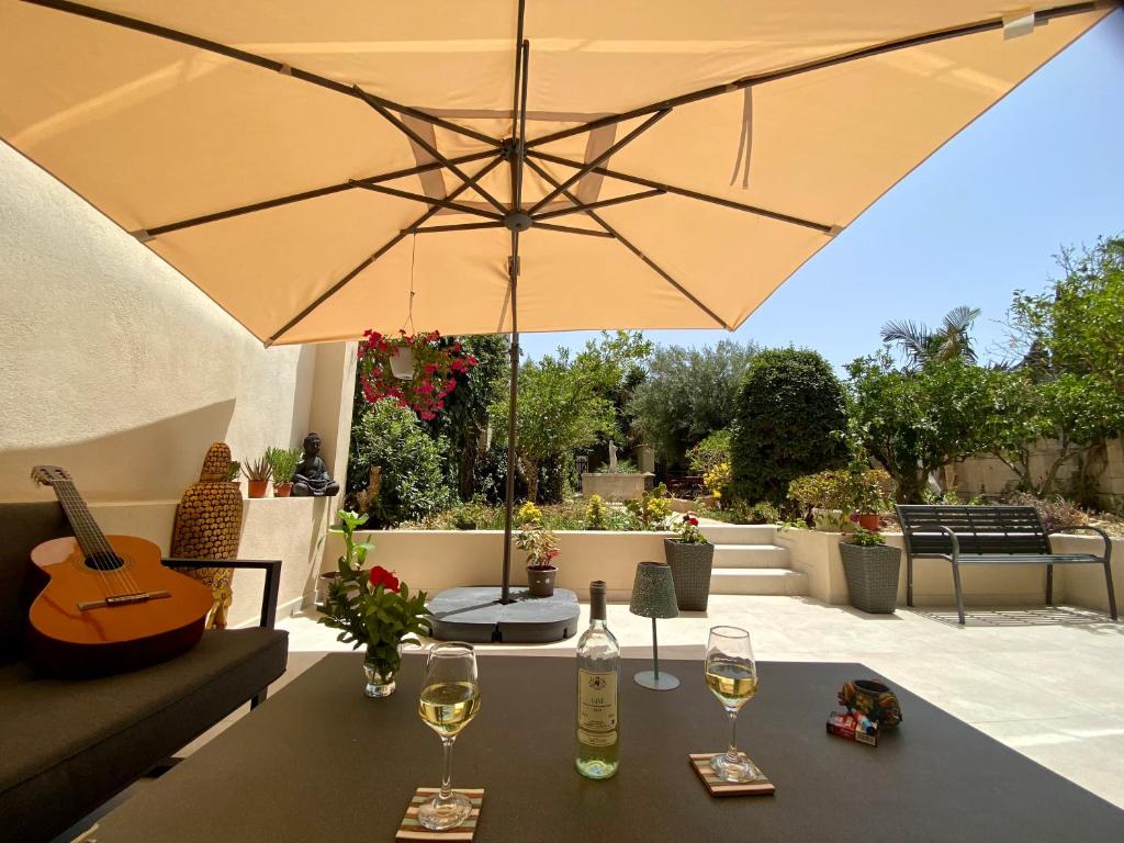 Maltese Garden Villa في موستا: طاولة مع كؤوس للنبيذ ومظلة على الفناء