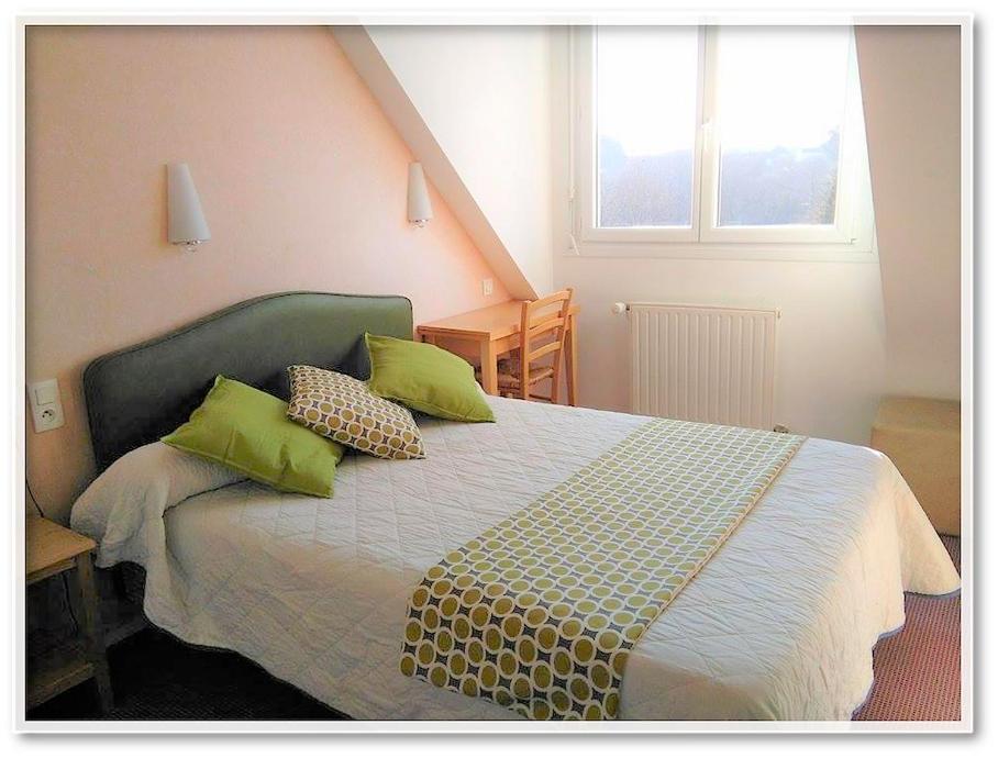 - une chambre avec un lit doté d'oreillers verts et d'une fenêtre dans l'établissement L'Orée du Bois, à Ergué-Gabéric