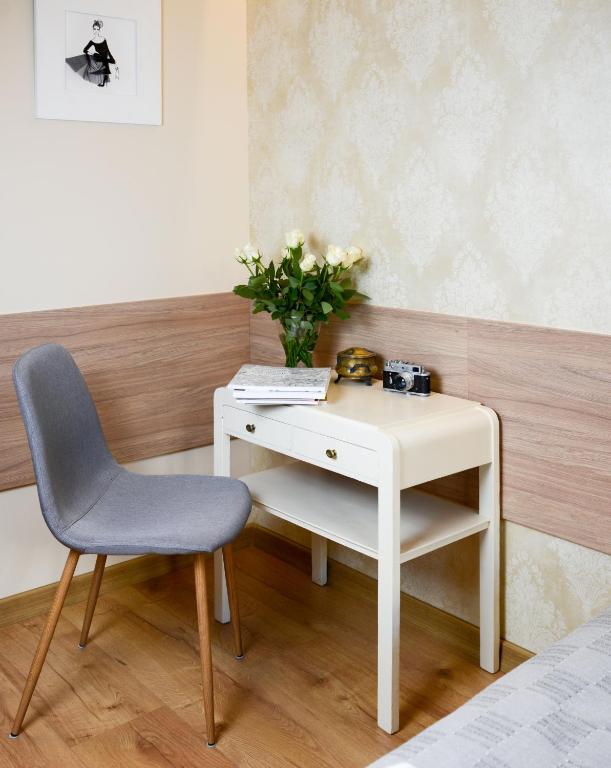 Compact cream desk with stack of books, vase of white roses, vintage camera, and gray chair