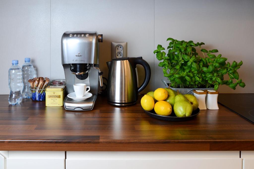Countertop coffee station with espresso machine, kettle, bottled water, fresh fruit, and basil plant, bright