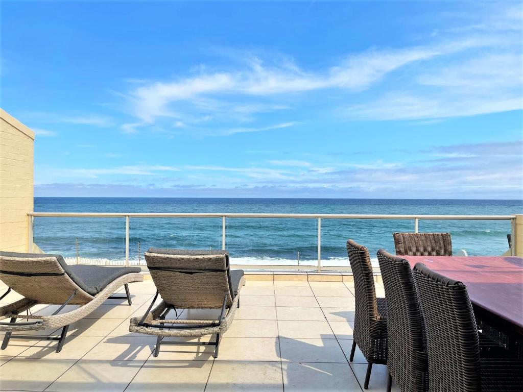 a patio with chairs and a table and the ocean at Beachfront @ Driftwood 6 Luxury Family Apartment in Ballito