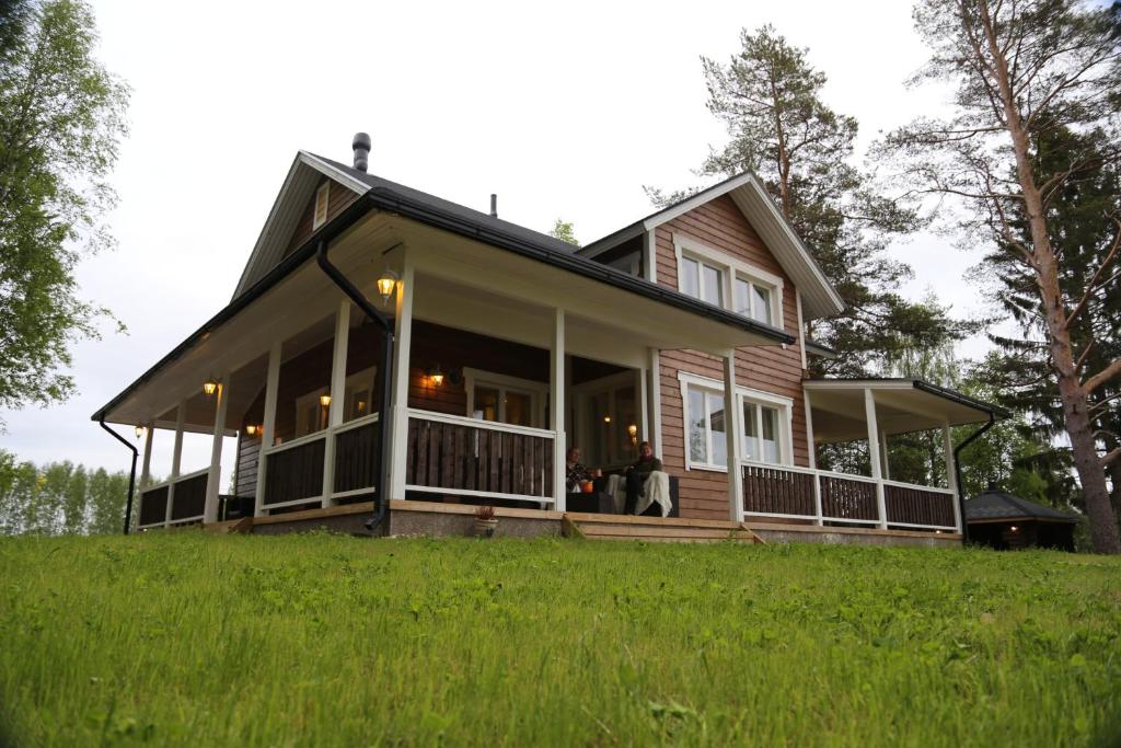 a house with a wrap around porch on a green field at Villa Haapaniemi in Iisalmi