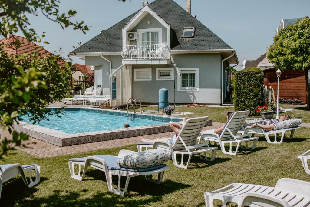 a backyard with a pool with chairs and a house at Kék Vendégház Family Resort in Gyenesdiás