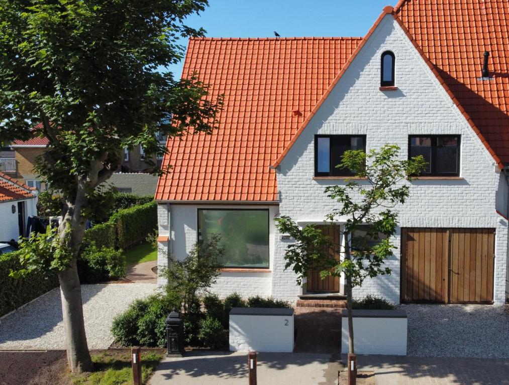 een wit huis met een oranje dak bij House Santa Maria in De Haan