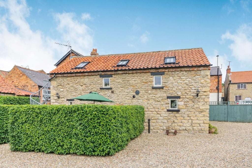 uma casa de pedra com uma sebe à sua frente em Upstairs Downstairs Cottage em Snainton