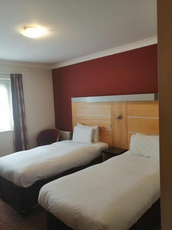 a hotel room with two beds and a chair at The Tudor Hotel in Harrow