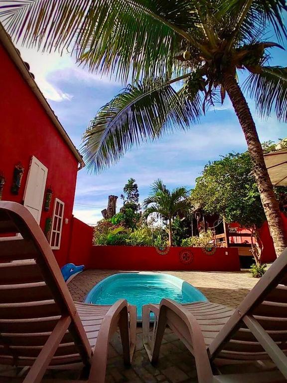a swimming pool with two chairs and a palm tree at Casa Vermelha Búzios in Búzios