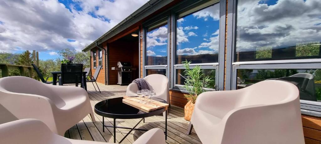 eine Terrasse mit weißen Stühlen, einem Tisch und Fenstern in der Unterkunft Kirkjubraut - Church street in Talknafjordur