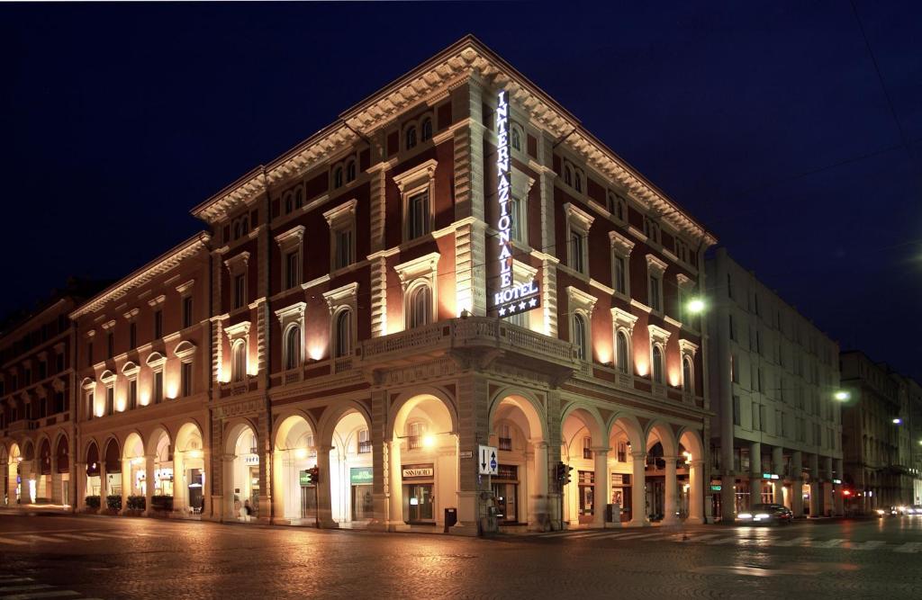 un grand bâtiment situé dans une rue de la ville la nuit dans l'établissement Hotel Internazionale, à Bologne