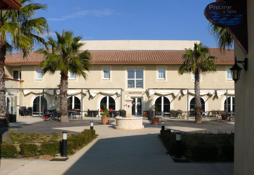 a large building with palm trees in front of it at Hôtel Jasses de Camargue in Gallargues-Le-Montueux