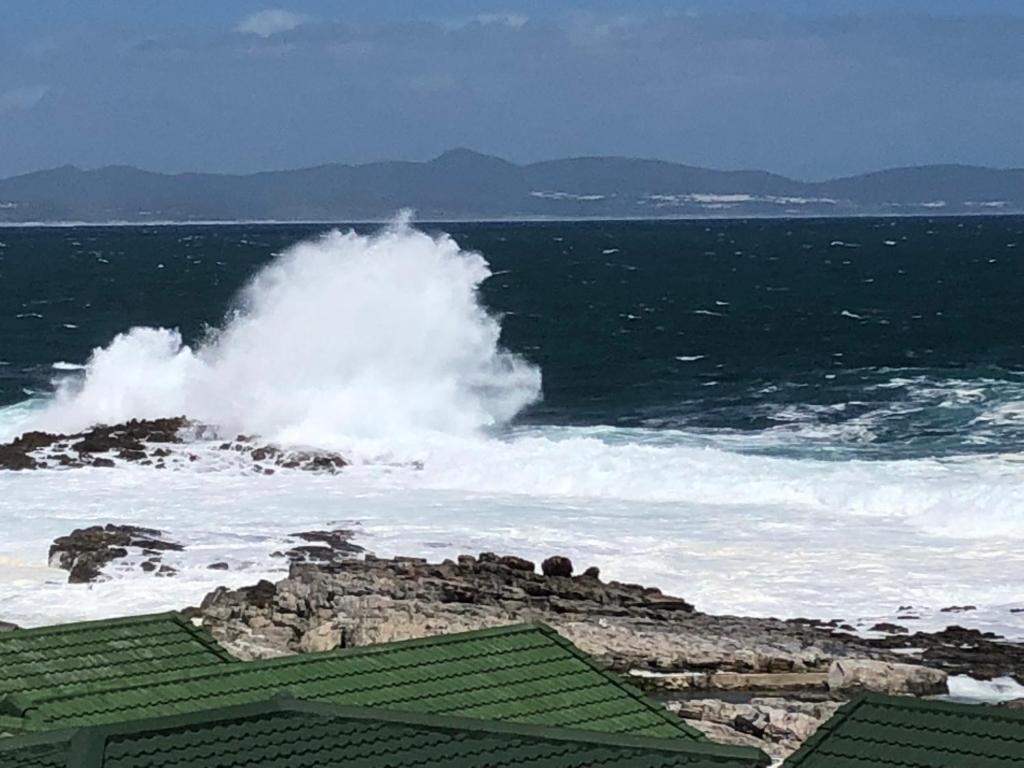 a large wave in the ocean with a building at Whale Rock Estate Hermanus sea view apartment in Hermanus