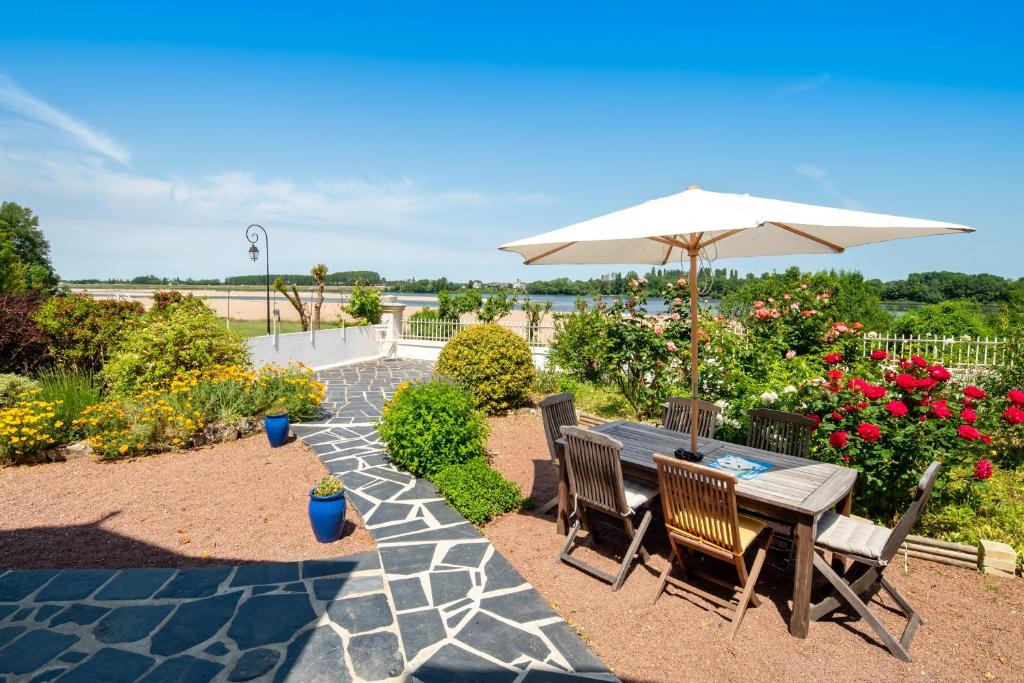 una mesa y sillas con sombrilla y flores en Le Clos Eugenie - Charmante maison avec jardin et vue sur la Loire, en Gennes