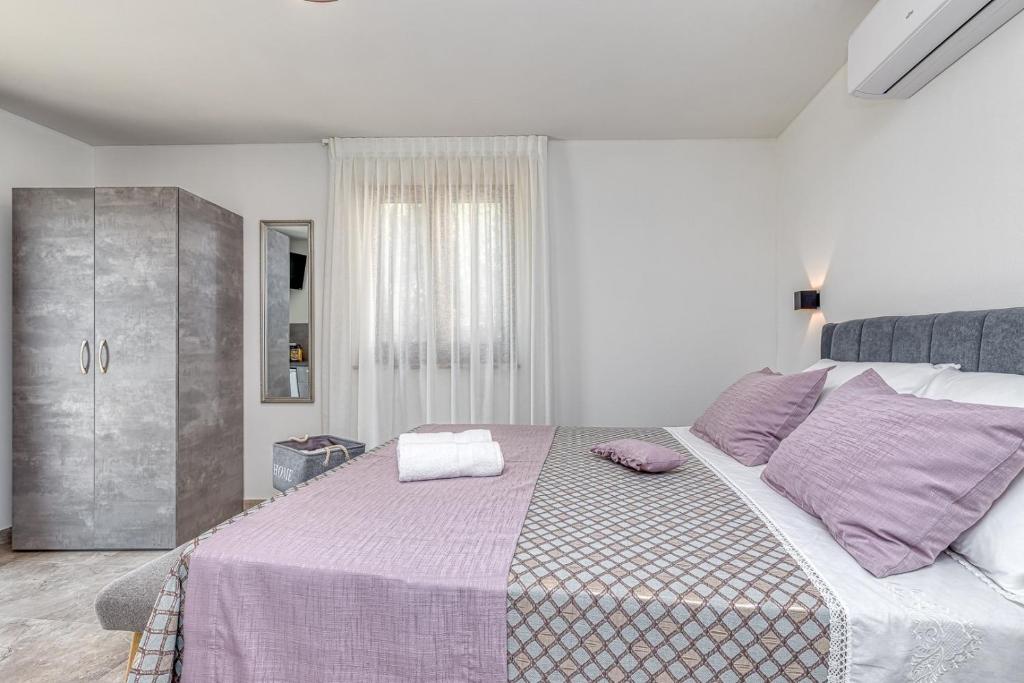 a white bedroom with a large bed with purple pillows at Rooms Nilda in Poreč