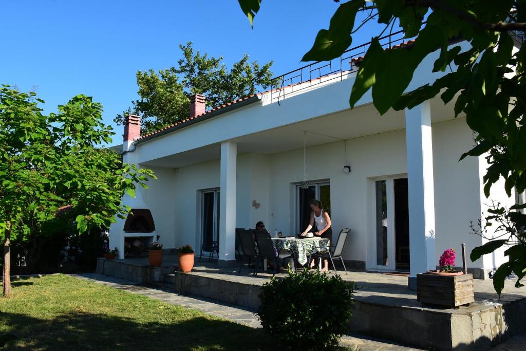 Eine Frau, die an einem Tisch vor einem weißen Haus sitzt. in der Unterkunft Villa Monte Kariotes in Samothráki