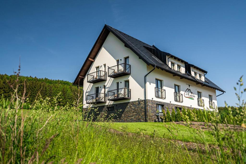 een groot wit huis met een zwart dak bij J-H APARTMÁNY HORSKÝ RESORT BUKOVÁ HORA - 100 m od LANOVKY in Červená Voda