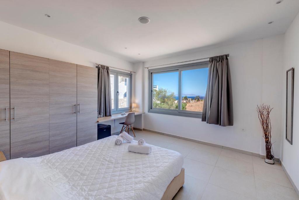 a white bedroom with a large bed and large windows at Chrysonisos Suites with Sunset & Seaviews near Kini in Ano Syros
