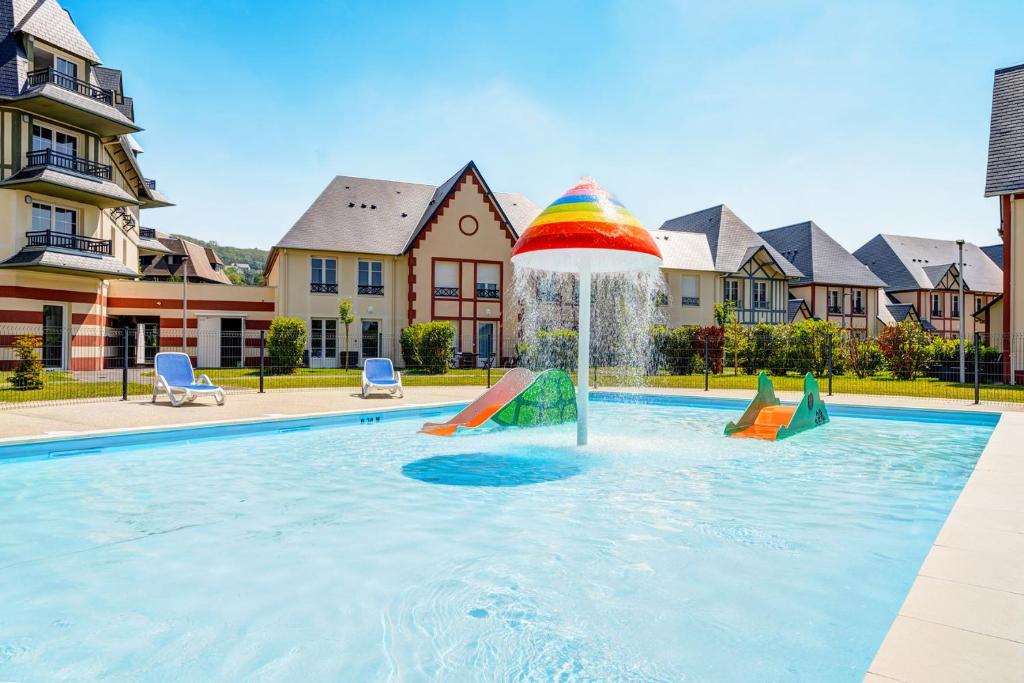 a pool with a fountain with a rainbow umbrella at Résidence Goélia Le Victoria in Blonville-sur-Mer
