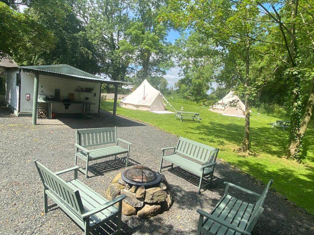 three park benches and a fire pit with tents at Duneden Belle Glamping in Randalstown