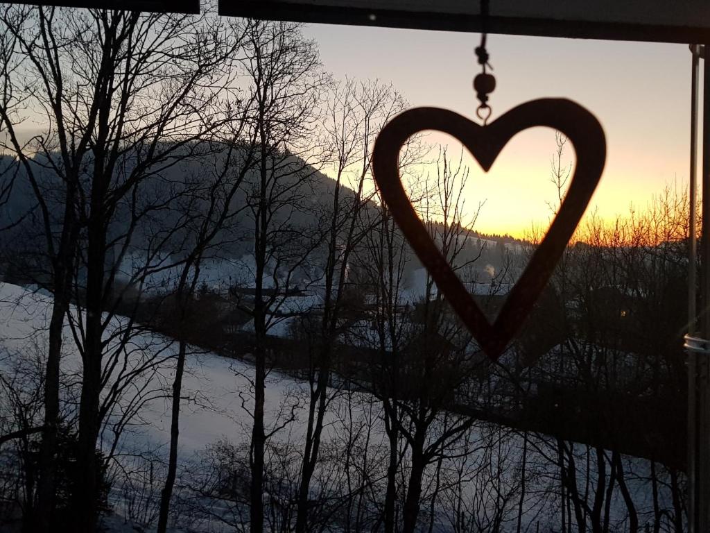 un cœur suspendu devant une fenêtre offrant une vue sur le coucher du soleil dans l'établissement Ferienwohnung im kuhlen Allgäu, à Missen-Wilhams