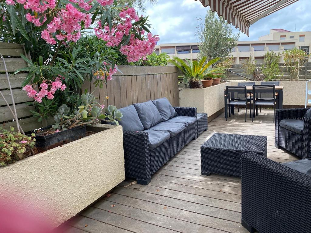 un patio con sofás, mesas y flores rosas en Appartement La Petite Maison, en Le Grau-du-Roi