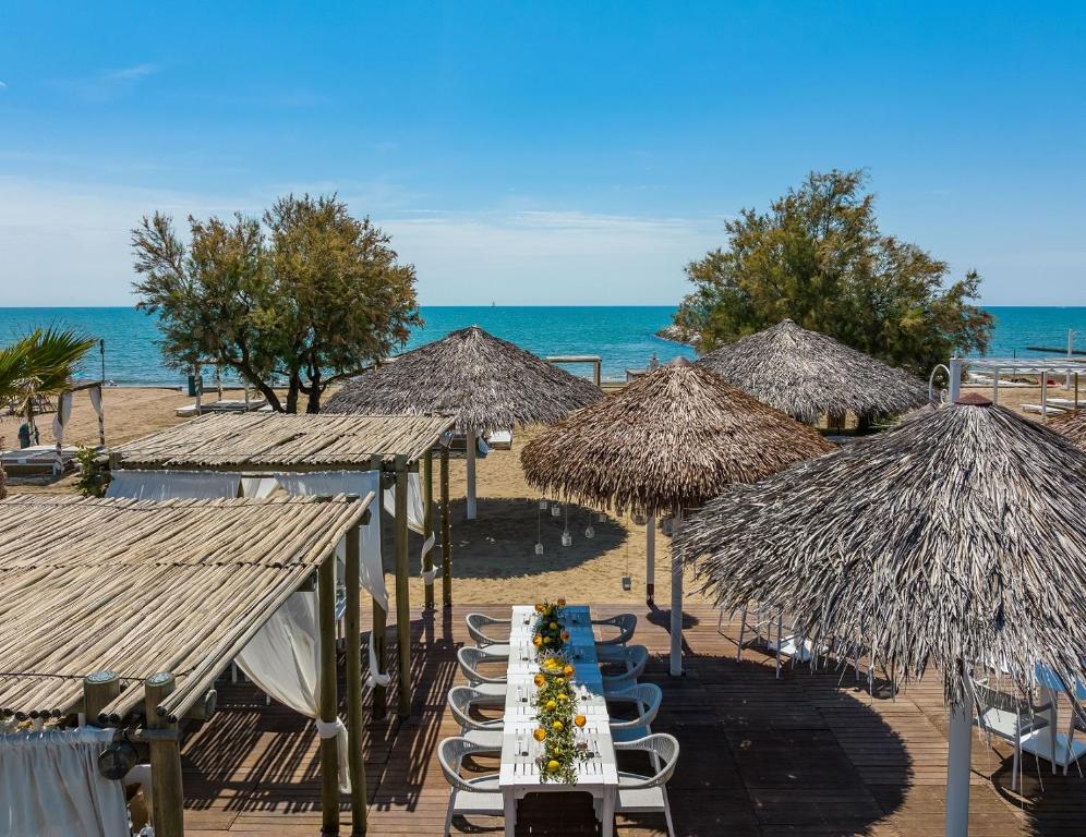 a table with chairs and straw umbrellas on a beach at Pareus Beach Resort in Caorle