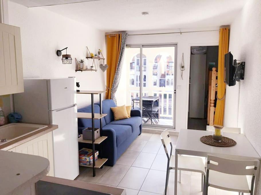 een keuken en een woonkamer met een blauwe bank bij Résidence Pointe Vermeille - Charmant Studio Cabine avec Jolie vue sur le lac marin in Le Barcarès