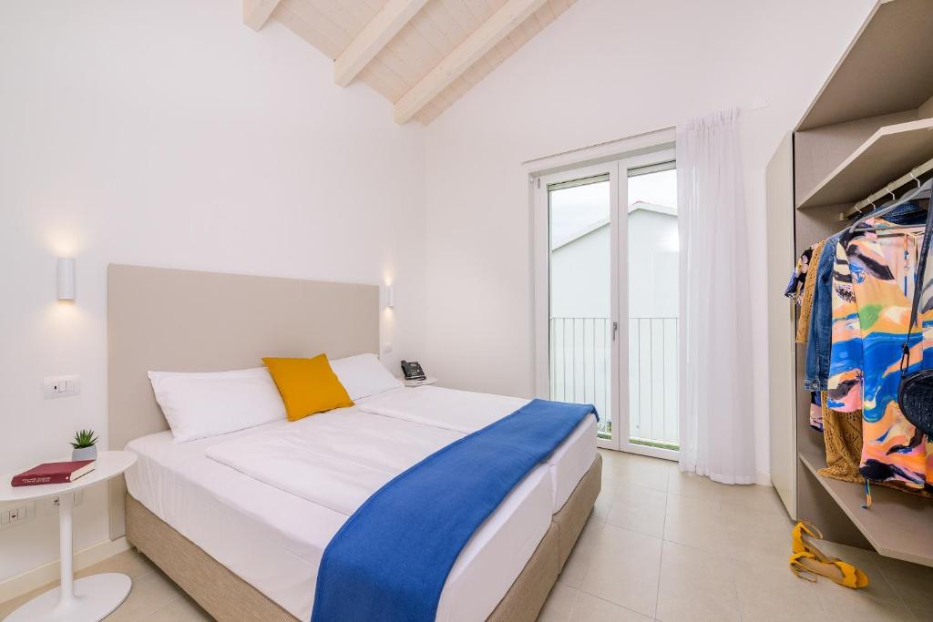 a white bedroom with a bed and a window at Pareus Beach Resort in Caorle