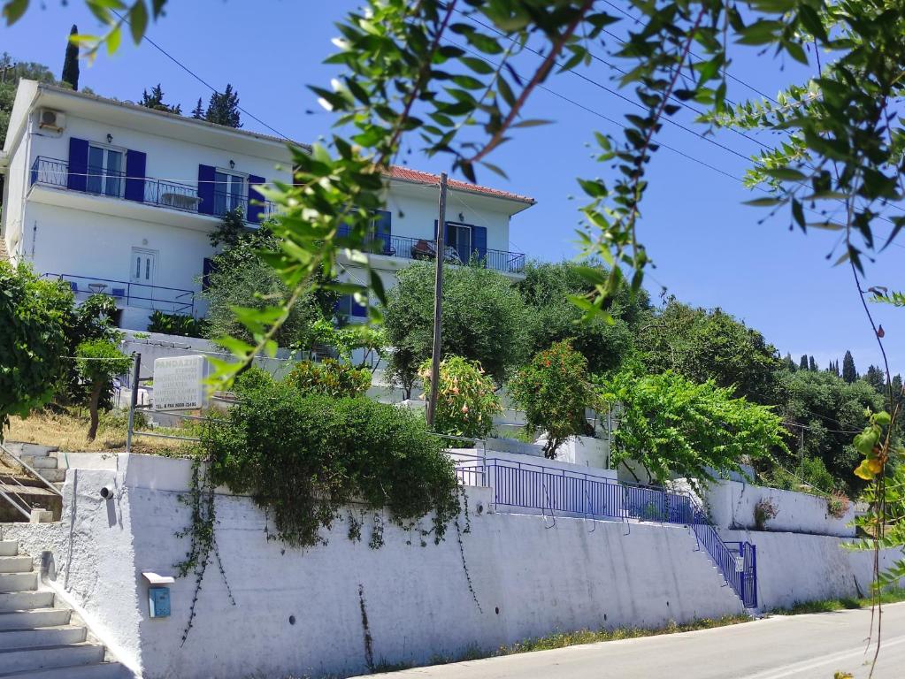 a building on top of a hill with trees at Blue and White Apartments in Benitses
