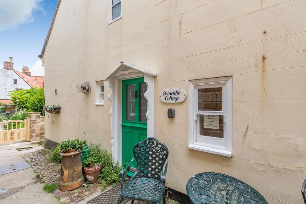 a building with a green door and two chairs at Brincliffe Cottage in Robin Hood's Bay