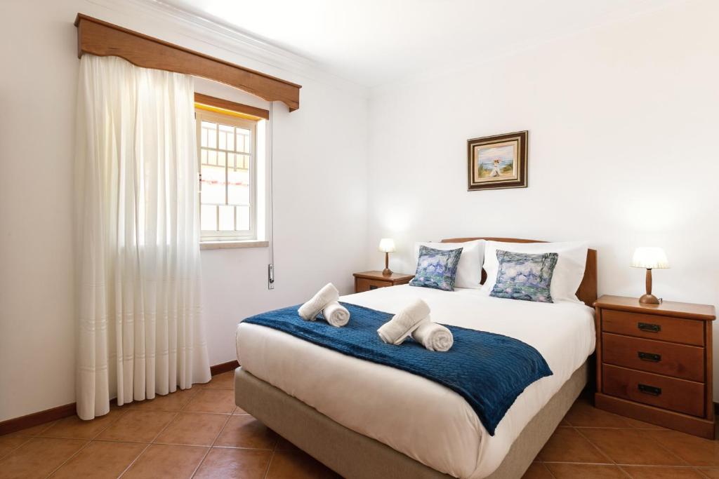 um quarto com uma grande cama branca com lençóis azuis em Village Beach House em Nazaré