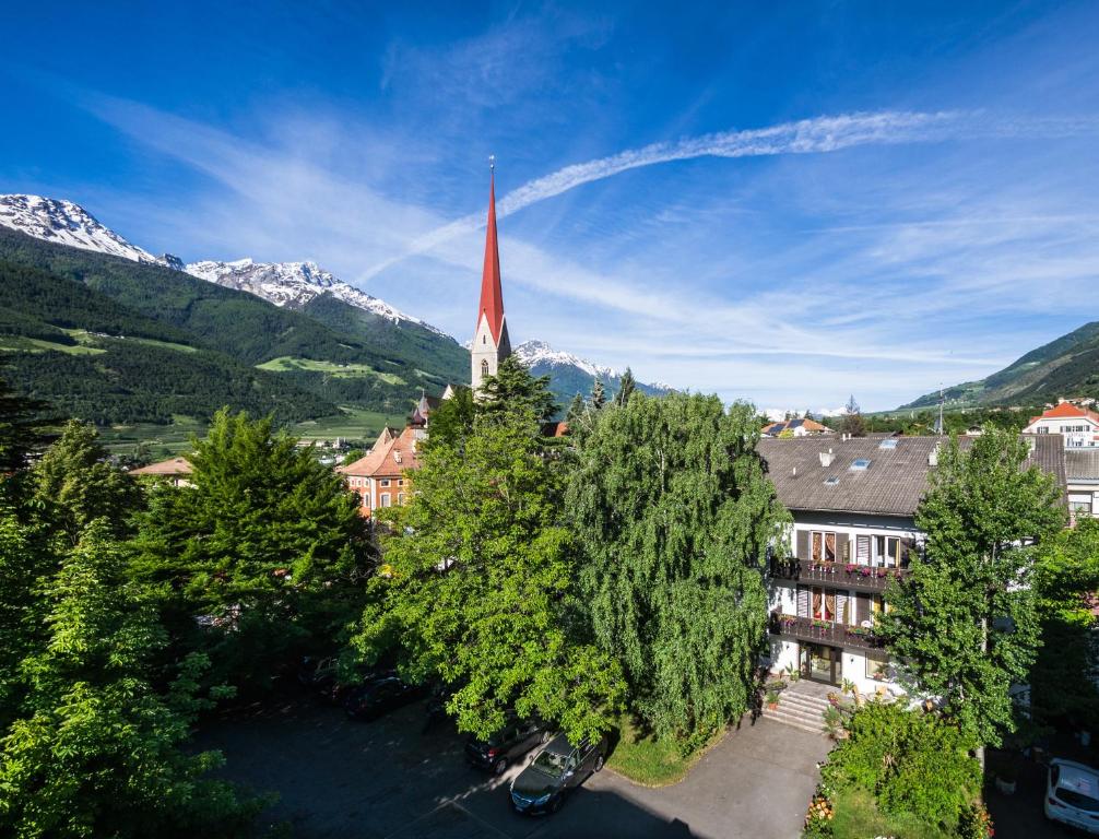 uma igreja com um campanário vermelho com montanhas ao fundo em Hotel Pension Schweitzer em Silandro