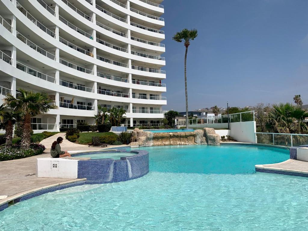 un hombre sentado frente a una piscina frente a un edificio en Beachfront 4 BR Penthouse - Pool Steps to Beach & Mins to Downtown, en Rosarito