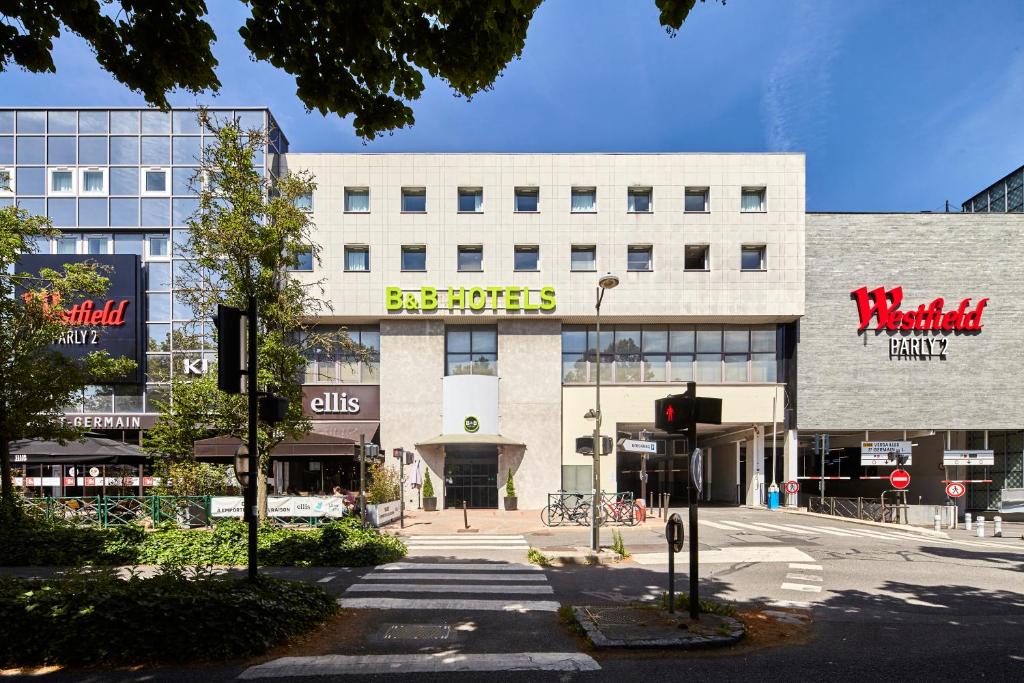 - un grand bâtiment blanc avec un panneau de magasins dans l'établissement B&B HOTEL Versailles Le Chesnay, à Le Chesnay