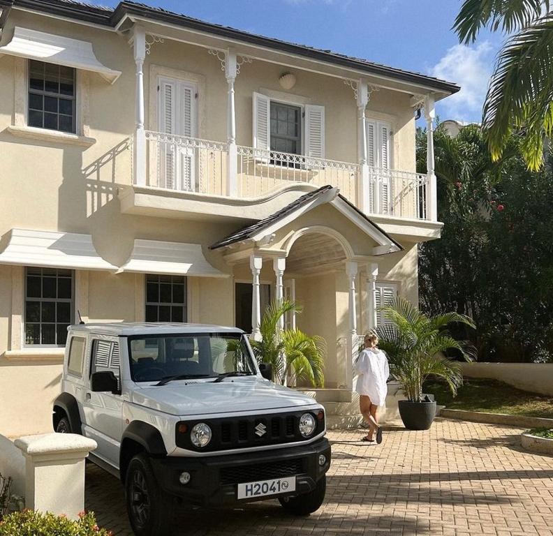 a woman standing in front of a house with a white truck at No5 Battaleys Mews Mullins Beach in Saint Peter