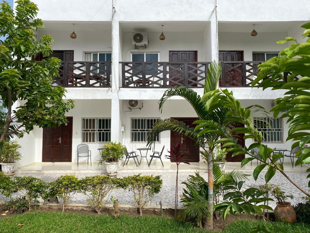 un edificio bianco con sedie e alberi di fronte di Queen Zee Garden Apartments a Kololi