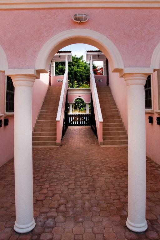 an archway leading up to a pink building with stairs at Sandy Bliss Condominiums in Saint James