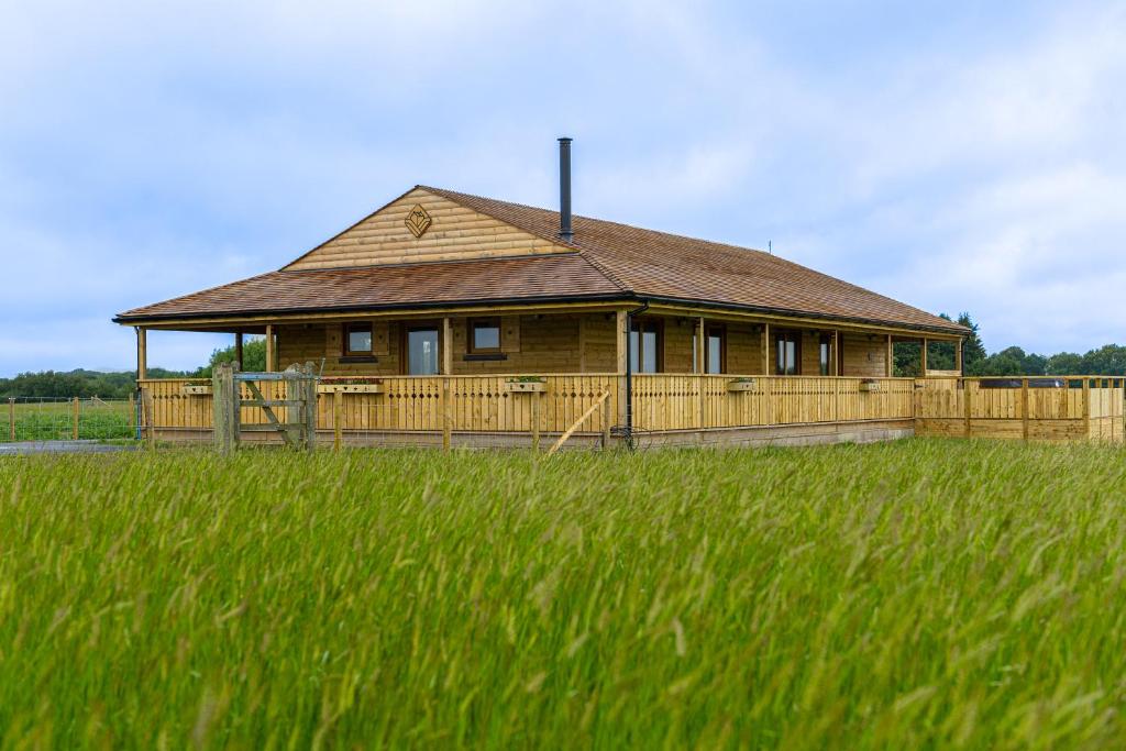 a large wooden house with a grass field in front of it at Luxury Log Cabin with a Hot Tub in Stone