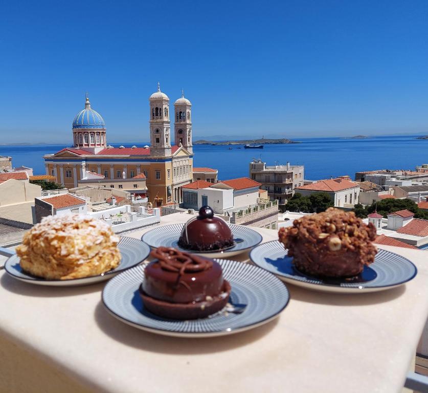 three cakes on plates on a table with a view of a city at Hermes Penthouse in Ermoupoli
