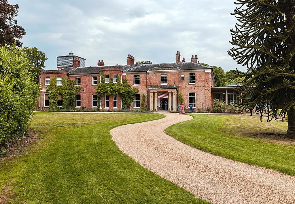 una gran casa de ladrillo rojo con un camino de tierra en The Retreat, Elcot Park en Newbury