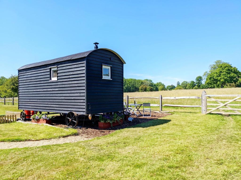 a black barn sitting in a field next to a fence at Crabden Shepherd Hut - Blendworth in Waterlooville