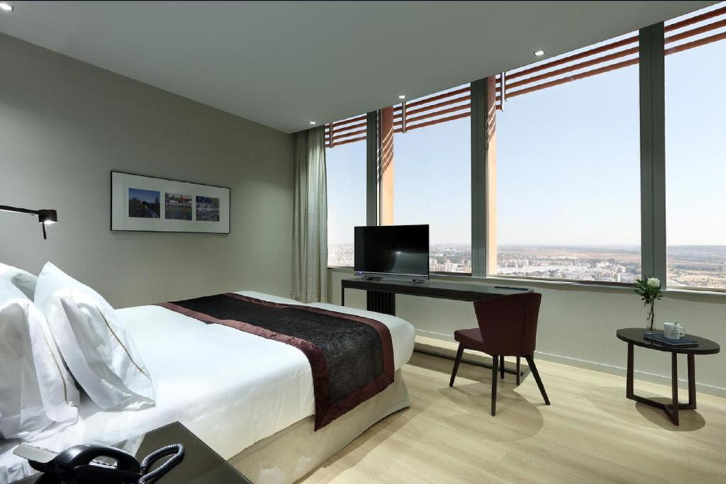 a bedroom with a bed and a desk with a television at Eurostars Torre Sevilla in Seville