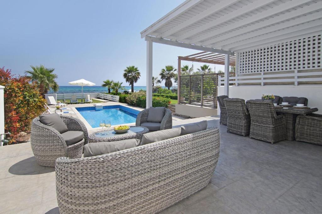 patio z wiklinowymi meblami i basenem w obiekcie Villa Aphrodisia - Seafront w Ajia Napa